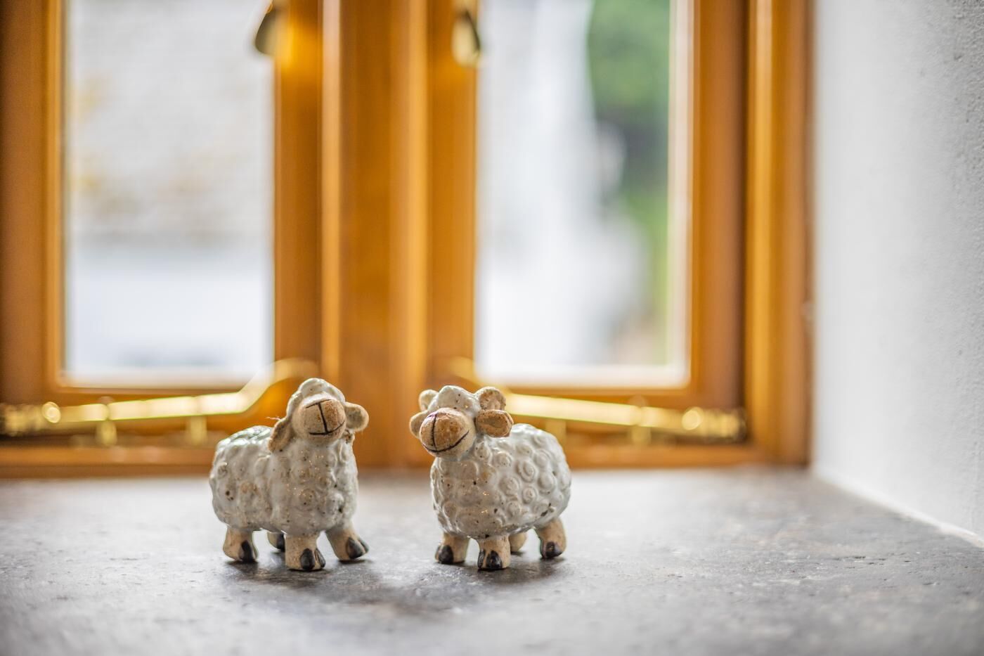 Zwei kleine Schaf-Figuren auf einer Ablage in der Nähe eines Fensters mit goldfarbenen Rahmen.
