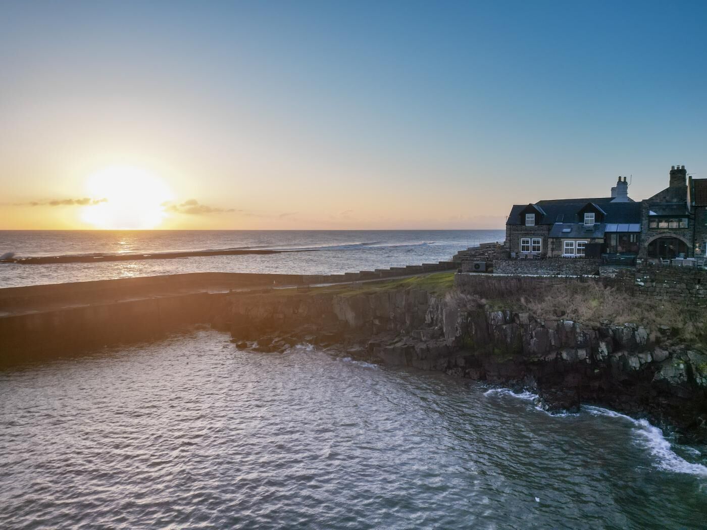A coastal property with a stone wall and a large house overlooking the sea.