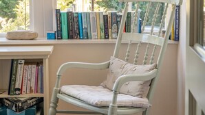 Una mecedora junto a una ventana con una estantería llena de libros.