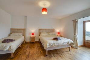 Une chambre avec deux lits, un plancher en bois et une grande fenêtre avec des rideaux.