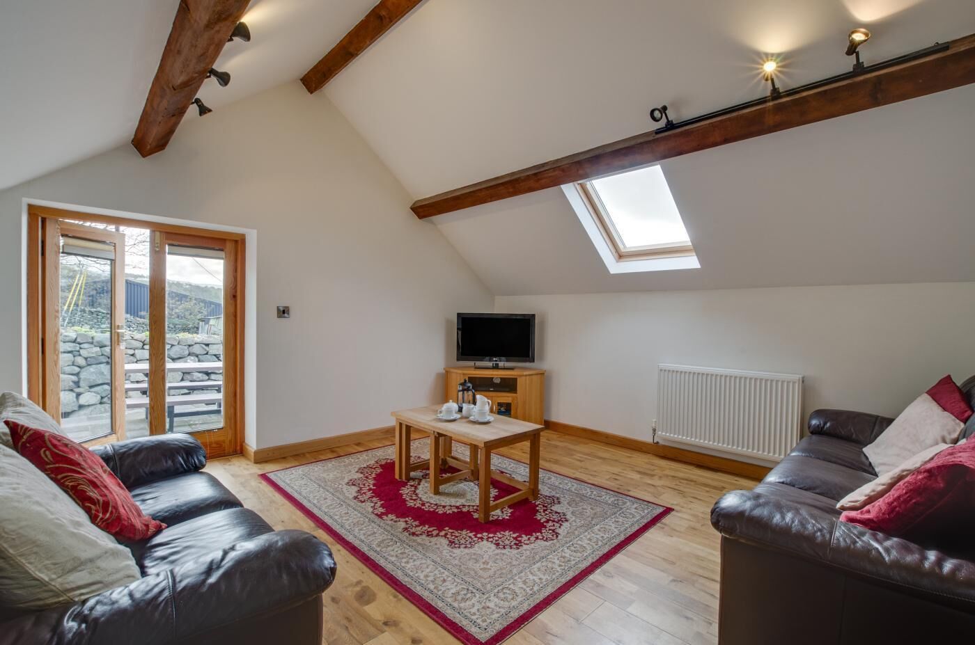 Una sala de estar acogedora con televisor, muebles de madera, un tapete rojo y un tragaluz.