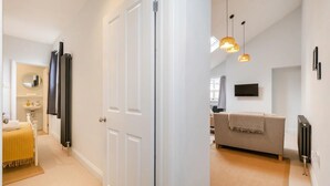 A hallway leading to a bathroom with a toilet, sink, and mirror. There is a sofa in the living area with a TV on the wall. - 1 Bed in Sheringham (oc-n33618) (Sheringham)