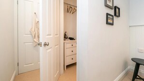 A hallway with a white door, a coat rack, a dresser with drawers, and framed pictures on the wall. - 1 Bed in Sheringham (oc-n33618) (Sheringham)
