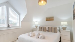 Un dormitorio con cama, lámparas de noche, una ventana con persianas, un radiador y un cuadro colgado en la pared.