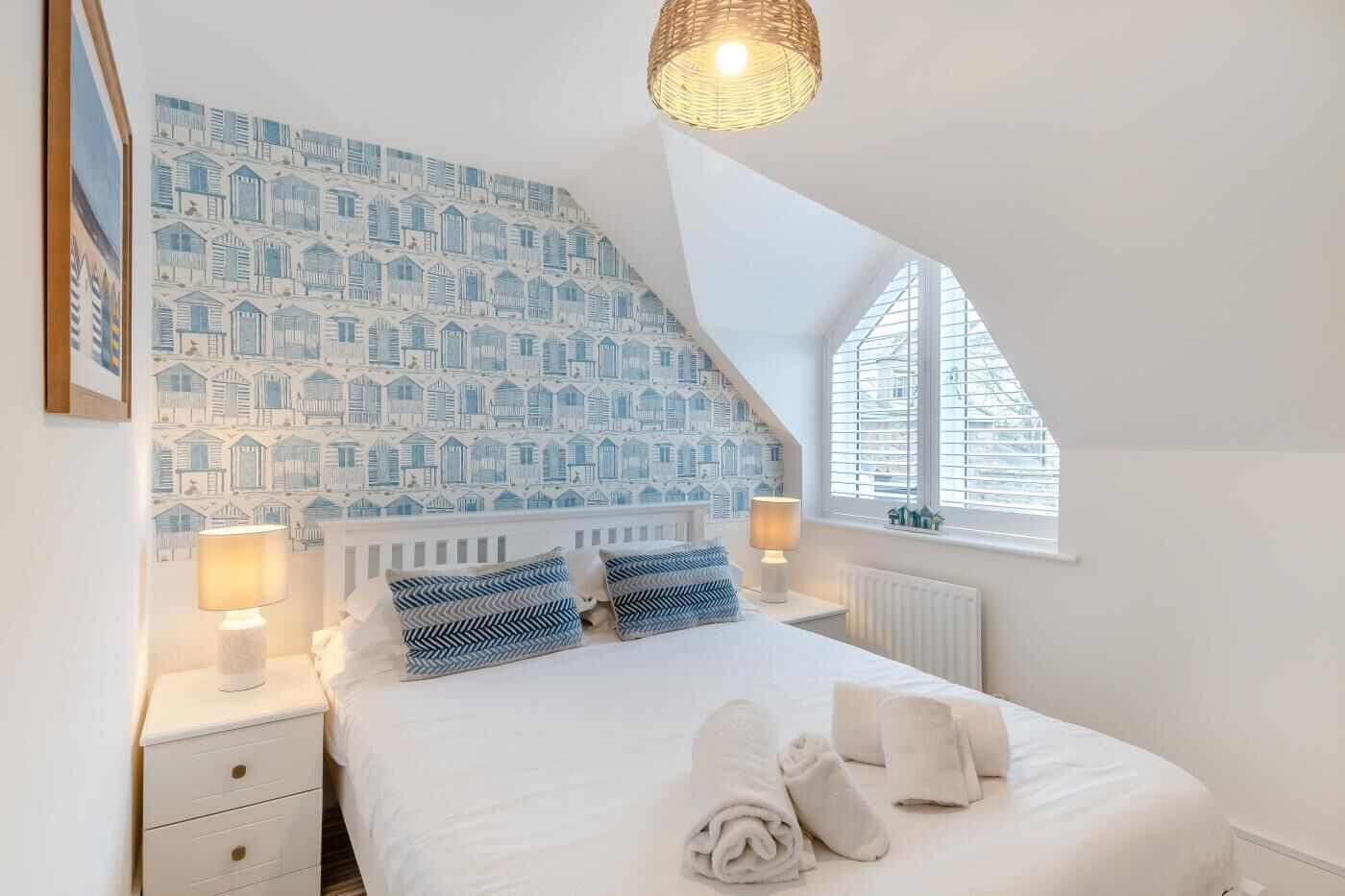 A bedroom with a sloped ceiling, a patterned wall, a bed with pillows, two bedside lamps, a window, and a radiator.