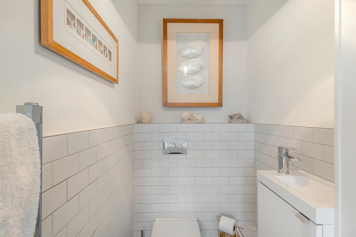 A bathroom with white tiled walls, a framed artwork above the sink, and a towel rack to the left.