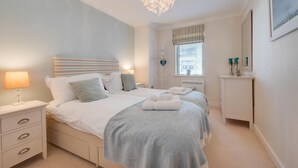 A bedroom with two beds, a chandelier, a bedside table with a lamp, a window with blinds, and a dresser with decorative items. - 2 Bed in Seahouses (oc-566411) (Seahouses)