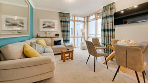 A living room with a sofa, chairs, a coffee table, and a TV mounted on the wall. - 2 Bed in Seahouses (oc-566411) (Seahouses)