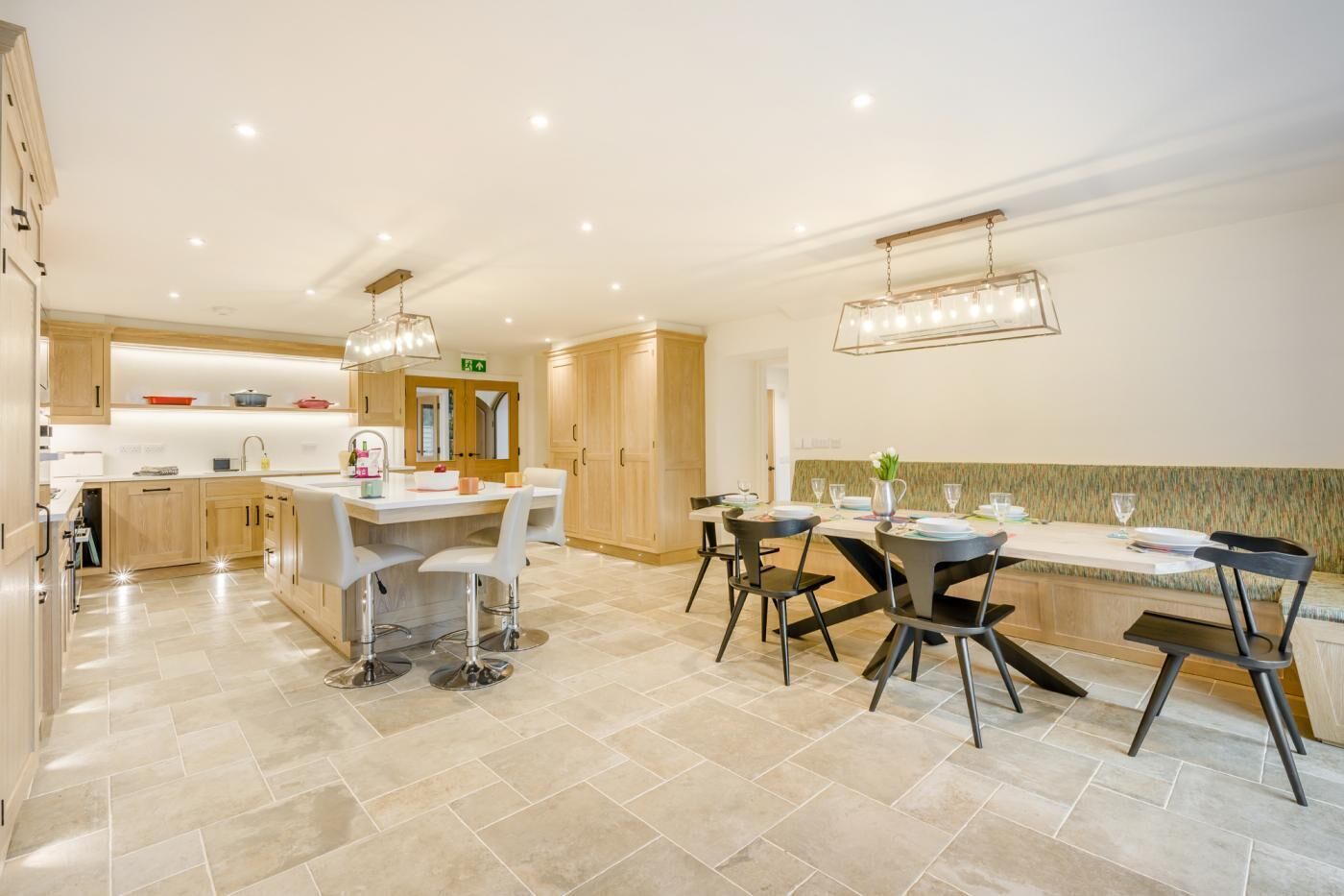 A modern kitchen with a central island, white bar stools, and a dining area with black chairs.