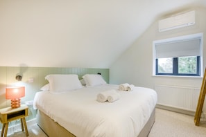 Une chambre à coucher avec un lit, des oreillers, une table de chevet avec une lampe, une fenêtre et un appareil de climatisation.