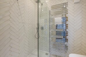 Une douche fermée par des parois en verre, dont les murs sont recouverts de carreaux disposés en motif de chevrons.
