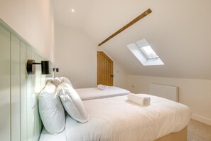 A bedroom with two beds, a skylight, a wooden door, and a radiator. - 4 Bed in Snettisham (oc-i33650) (Snettisham)