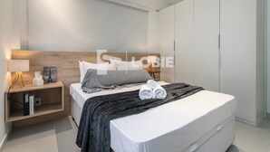 A modern bedroom with a wooden headboard, a bedside table with a lamp, and a neatly made bed with rolled towels. - Lobie Vilares Copacabana (Rio de Janeiro)