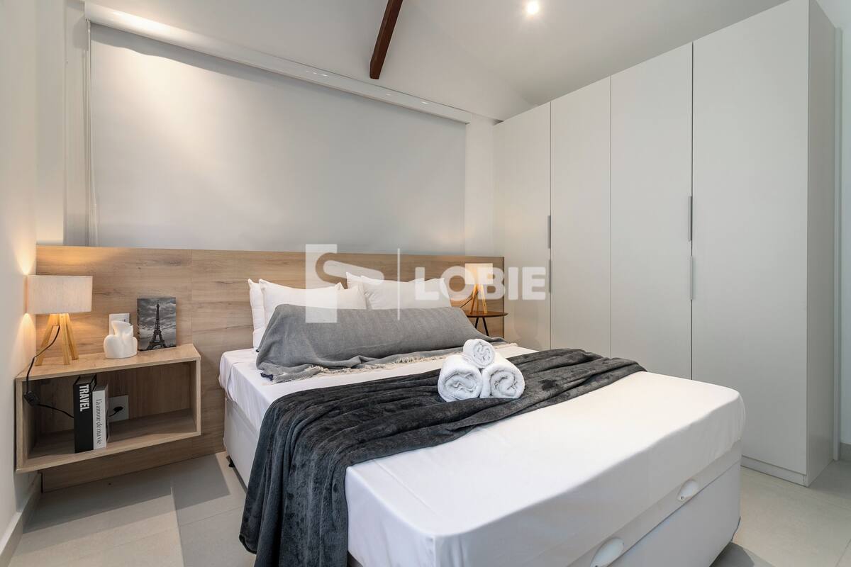 Una camera da letto moderna con una testiera in legno, un comodino con una lampada e un letto rifatto con asciugamani arrotolati.