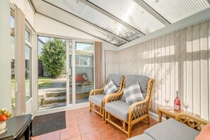 A sunroom with wicker furniture, a glass door leading outside, and a small table with a bottle and glass.