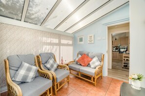 A room with two wicker sofas, a small table, and a kitchen in the background.