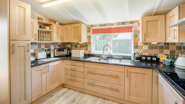Una cocina con armarios de madera, encimera negra, ventana con persiana roja y salpicadero de azulejos.