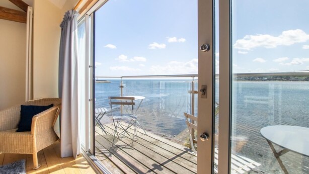 Een balkon met uitzicht op zee, een rieten stoel en een tafel.