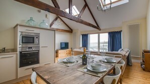 Een moderne keuken met een eethoek, houten balken en uitzicht op zee.