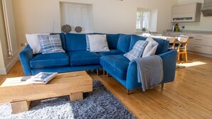 Een woonkamer met een blauwe hoekbank, een houten salontafel en een grijze vloerkleed.