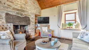 A cozy living room with a stone fireplace, comfortable seating, a flat-screen TV, and a window with curtains. - 1 Bed in Wick (oc-b33442) (Wick)