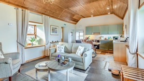 A cozy living room with a sofa, coffee table, and a dining area. A kitchen with green cabinets is visible in the background. - 1 Bed in Wick (oc-b33442) (Wick)