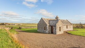 A stone cottage with a gravel driveway, surrounded by open fields and a clear sky. - 1 Bed in Wick (oc-b33442) (Wick)