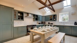 A modern kitchen with teal cabinets, a central island, and a dining table set for six. - 4 Bed in nr Beadnell (oc-566760) (Beadnell)