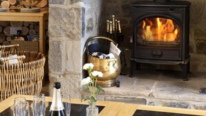 A cozy room with a stone fireplace, a table with wine glasses, and a wicker chair. - 4 Bed in nr Beadnell (oc-566760) (Beadnell)