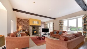 A spacious living room with two sofas, a fireplace, a television, and a stone wall. - 4 Bed in nr Beadnell (oc-566760) (Beadnell)