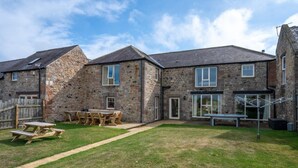 A stone house with a grassy yard, a wooden picnic table, and a clothes drying rack. - 4 Bed in nr Beadnell (oc-566760) (Beadnell)