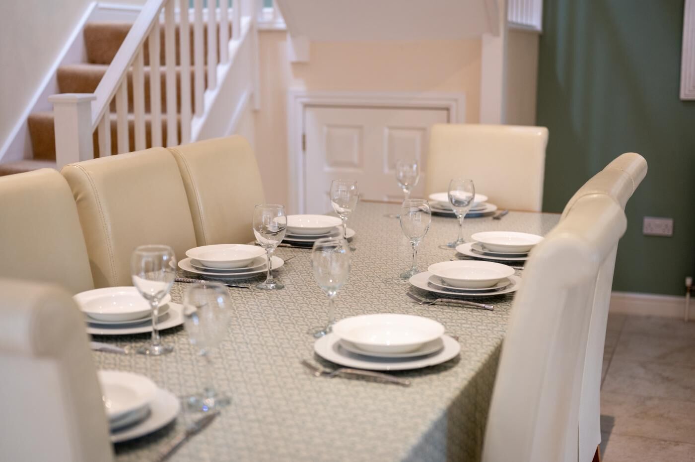A dining table set for six with white plates, glasses, and cutlery.
