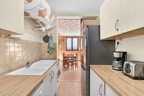 A kitchen with a sink, washing machine, wooden table, and a refrigerator. - Apartment 'Orcières Village' with Mountain View and Balcony (Orcières)