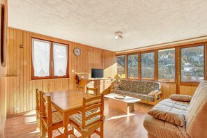 A wooden interior with a dining table, chairs, a sofa, and large windows. - Apartment 'Orcières Village' with Mountain View and Balcony (Orcières)