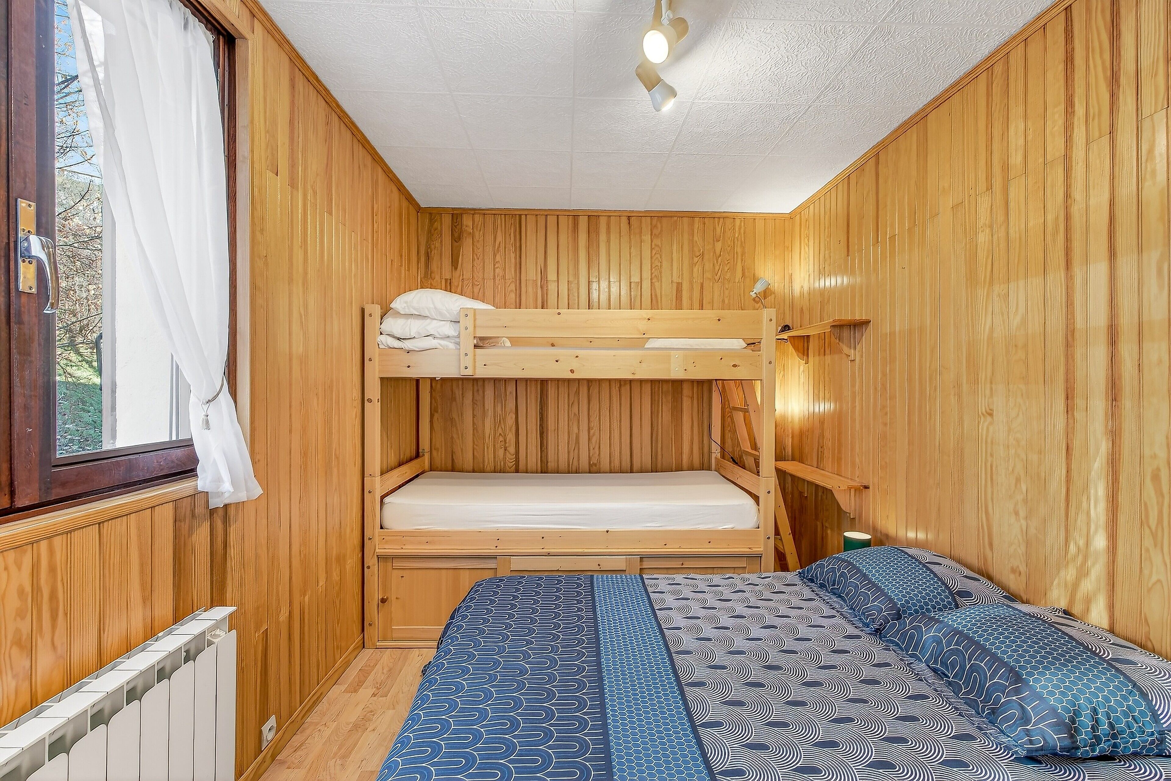 Una habitación de madera con literas, una ventana con cortinas y un radiador.