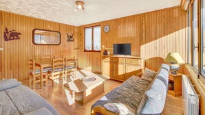 Um quarto com painéis de madeira, um sofá, uma mesa de jantar com cadeiras, uma televisão e uma janela.