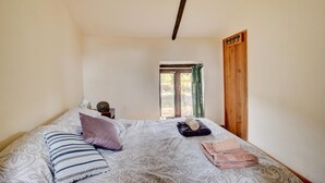 Een slaapkamer met een bed, kussens, een nachtkastje, een raam en een houten deur.