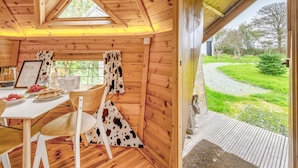 A cozy wooden cabin with a dining area, a table set with food, and a view of a grassy path outside. - 1 Bed in Redberth (oc-h33668) (Redberth)