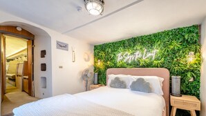 A bedroom with a bed, a wall-mounted plant wall, a ceiling fan, and a bedside table with a lamp.