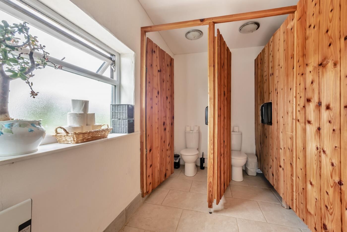 Un couloir étroit aux murs en bois, une fenêtre avec une plante et un lavabo sur lequel est posé un panier.