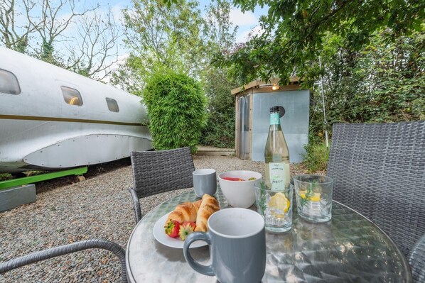 A table set outdoors with a croissant, a bottle of sparkling wine, and glasses.