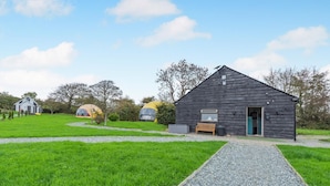 A rustic cabin with a gravel path leading to it, surrounded by green grass and trees.