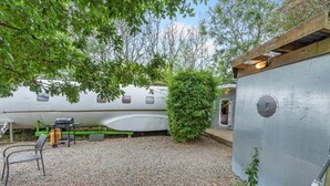 A small airplane converted into a home with a gravel patio, a grill, and a green bush.