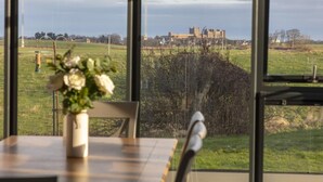A room with a large window overlooking a castle and a grassy field. - 2 Bed in Bamburgh (oc-nb1969) (Bamburgh)