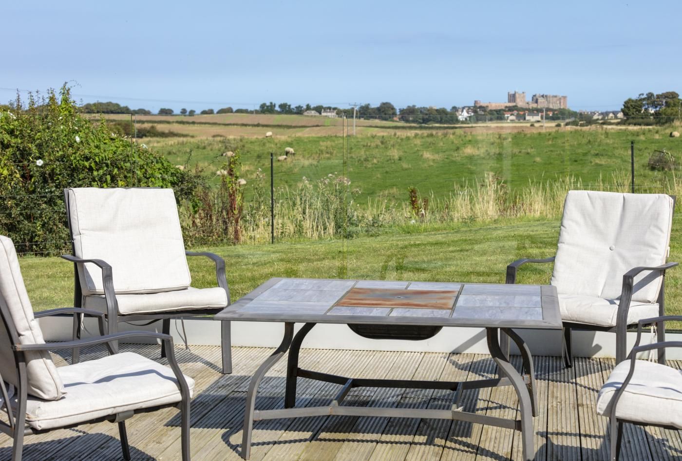 An outdoor seating area with a table and chairs, overlooking a grassy field and a distant castle.