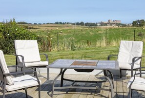 An outdoor seating area with a table and chairs, overlooking a grassy field and a distant castle. - 2 Bed in Bamburgh (oc-nb1969) (Bamburgh)
