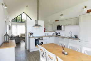 A modern kitchen with white cabinets, a wooden dining table, and a large window providing natural light. - 2 Bed in Bamburgh (oc-nb1969) (Bamburgh)
