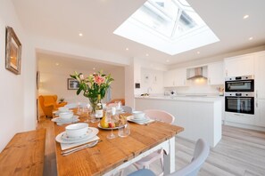 A modern kitchen with white cabinets, a dining table set with plates, glasses, and a vase of flowers. - 3 Bed in Beer (oc-t33690) (Beer)