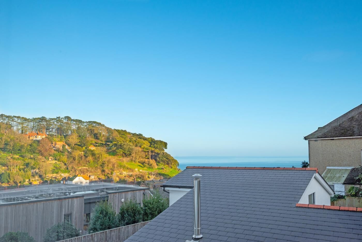 A residential rooftop with a view of a hillside and the sea.
