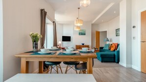 A modern dining area with a wooden table set for four, a bench, and a TV in the background. - 2 Bed in Swanage (oc-wy619) (Swanage)